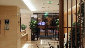 A hotel lobby with a reception desk, potted plants, and a glass door leading to the entrance. - Meihao EZZI Hotel (Tianjin Youyi Road Wudadao) (Tianjin)
