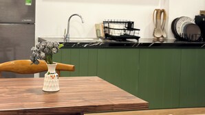A kitchen with a dining table, chairs, a hanging light fixture, and shelves with potted plants.