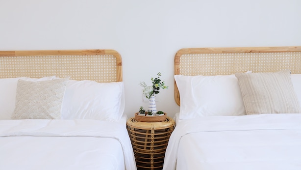 A double bed with a woven headboard, white bedding, and a small side table with a vase of flowers.