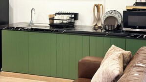 A modern kitchen with green cabinetry, a black countertop, and a brown leather sofa.
