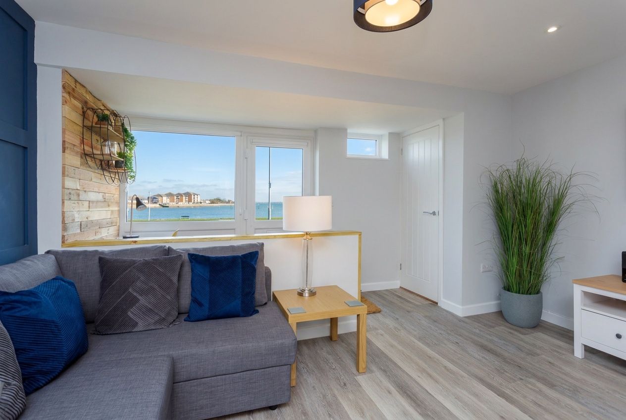 A modern living room with a sofa, a lamp, a potted plant, and a view of the sea.