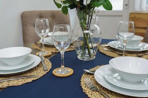 Et spisebord dækket med hvide tallerkener, blanke glas og en vase med grønne blade.