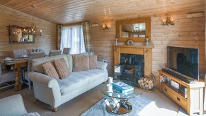 Ein gemütliches Cabin-Interieur mit einer Couch, einem Glastisch, einem Kamin und einem Fernseher.