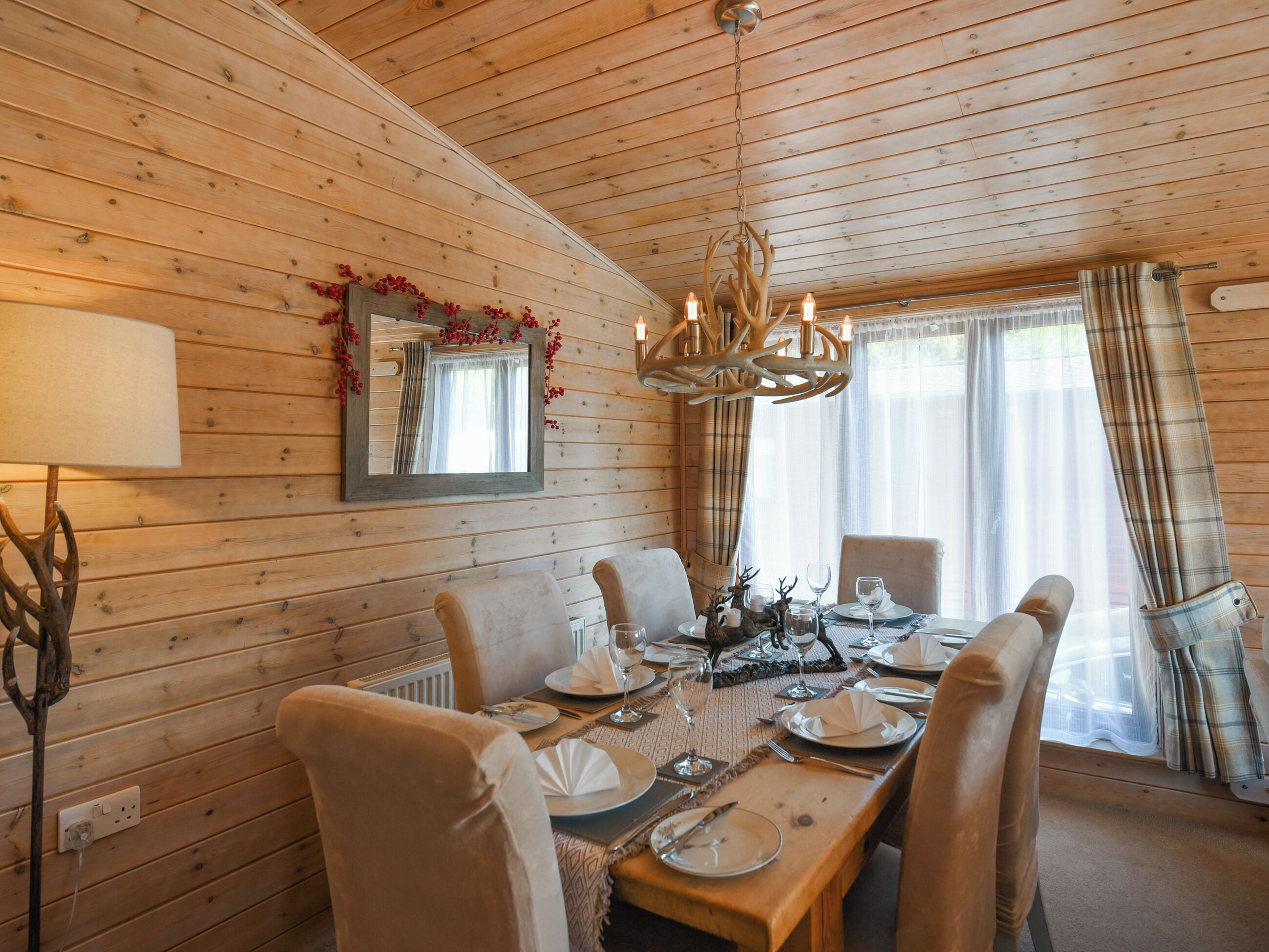 A wooden-paneled dining room with a chandelier, a mirror, and a table set for six.