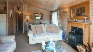 Ein gemütliches Blockhaushaus-Interieur mit einer Couch, einem Glastisch, einem Kamin und einer Küchenzeile.