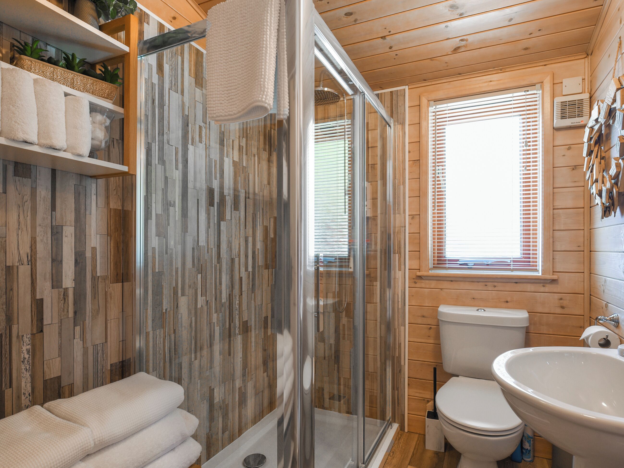 A wooden cabin bathroom with a shower, toilet, and sink.