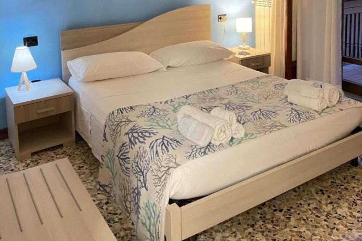 A hotel room with a bed, nightstands, a painting, and a view of the outside.
