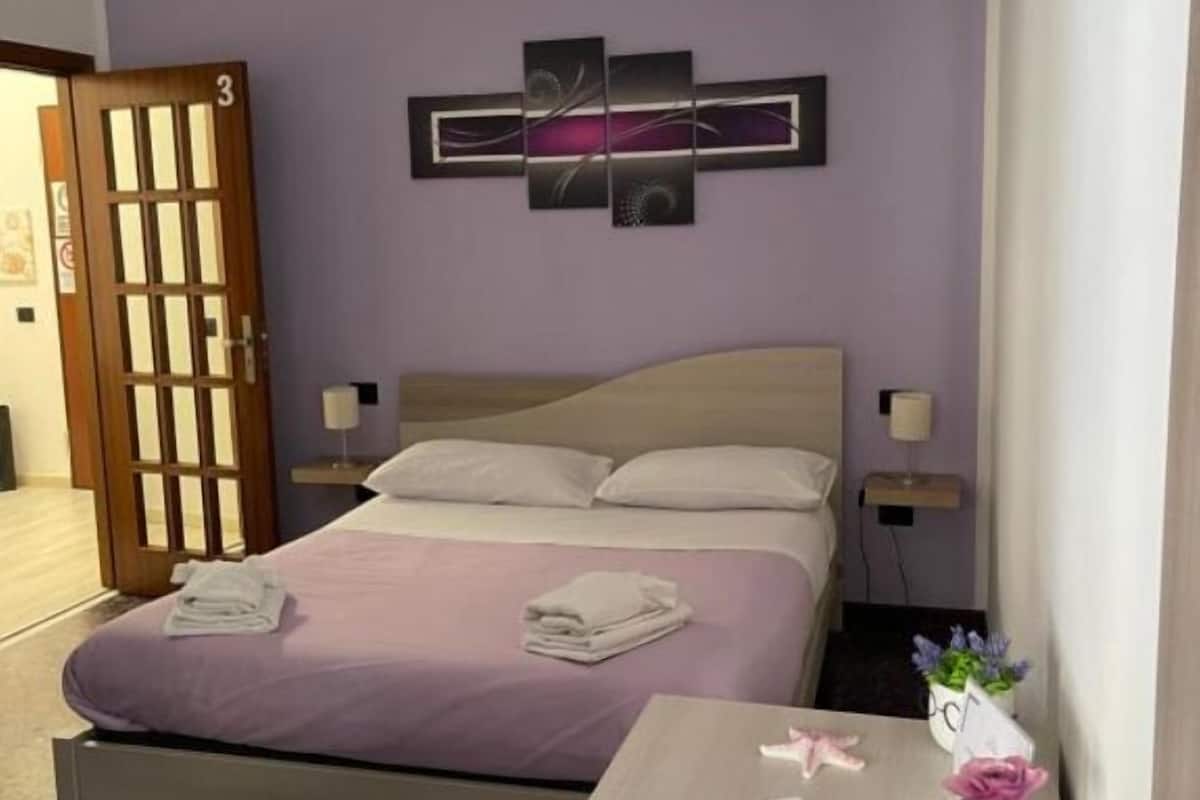 A hotel room with a bed, bedside tables, a wall-mounted artwork, and a door.