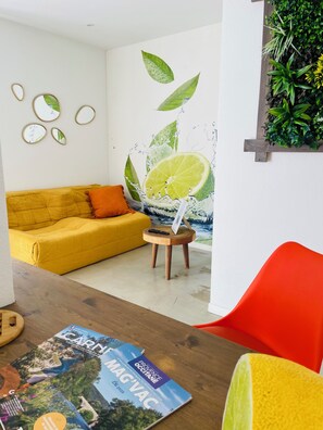 Ein Zimmer mit einem gelben Sofa, einem roten Sessel, einem Holztisch mit Zeitschriften und einer Wandmalerei von einer Limettenscheibe.