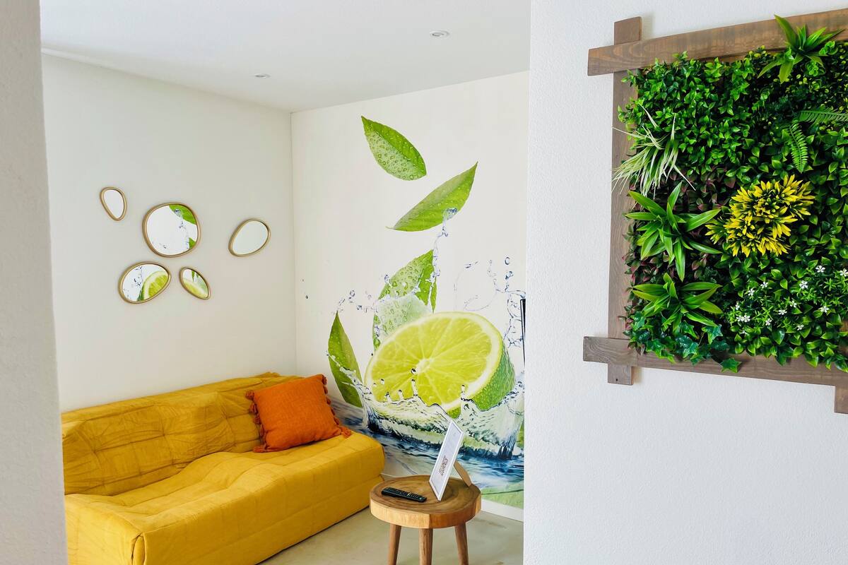 A room with a yellow sofa, a wall-mounted mirror, and a wall art depicting a lime slice with water splashes.