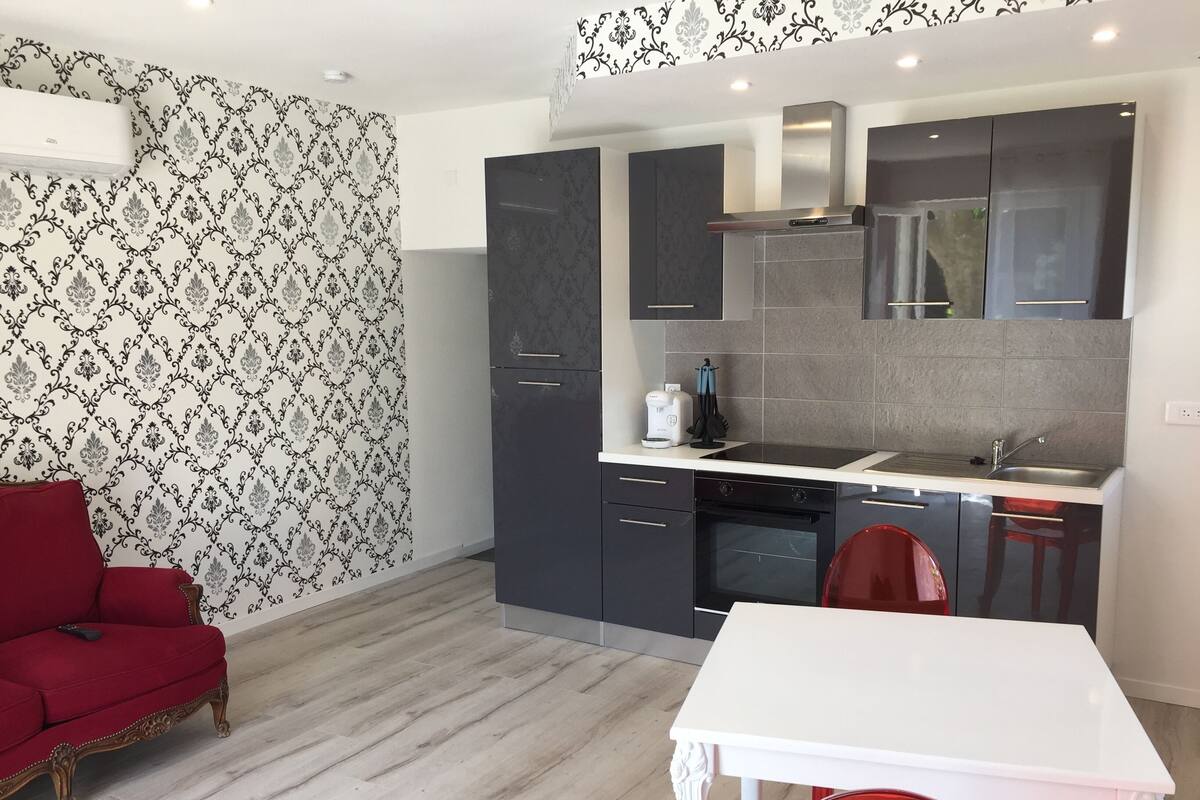 A modern kitchen with grey cabinets, a white countertop, and a red chair.