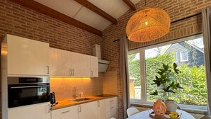 A modern kitchen with white cabinets, a black microwave, and a wooden floor. There is a round table with chairs and a hanging light fixture. - Villa Frans -Gezellige bungalow in Renesse (Renesse)