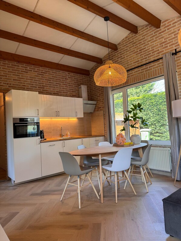 A modern kitchen with white cabinets, a wooden dining table, and a hanging light fixture.