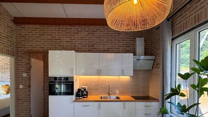 A modern kitchen with white cabinets, a large round table, and a hanging wicker light fixture. - Villa Frans -Gezellige bungalow in Renesse (Renesse)