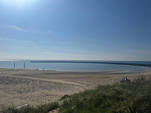 A beach with a clear sky, calm water, and a distant pier.