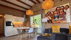 A modern kitchen with white cabinets, a dining area with a table and chairs, and a living room with a sofa and cushions. - Villa Frans -Gezellige bungalow in Renesse (Renesse)