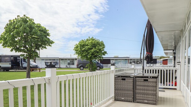 Une terrasse extérieure couverte, agrémentée d’une clôture blanche, de deux paniers en osier et d’un arbre en arrière-plan.