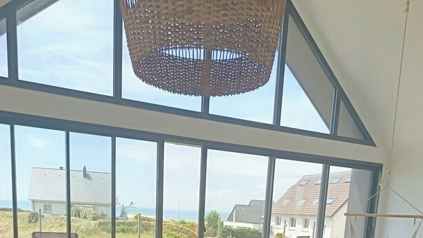 En moderne stue med et stort vindue, et spisebord med stole, en sofa og en hængestol.