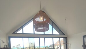 En rummelig opholdsstue med højt til loftet, store vinduer, et spisebord med stole, en sofa og en hængende lampe.