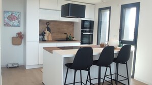 Et moderne køkken med en central ø, sorte barstole og integreret hårde hvidevarer.