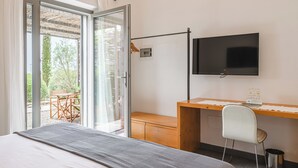 A hotel room with a bed, a desk with a chair, a television, and a sliding glass door leading to an outdoor seating area.
