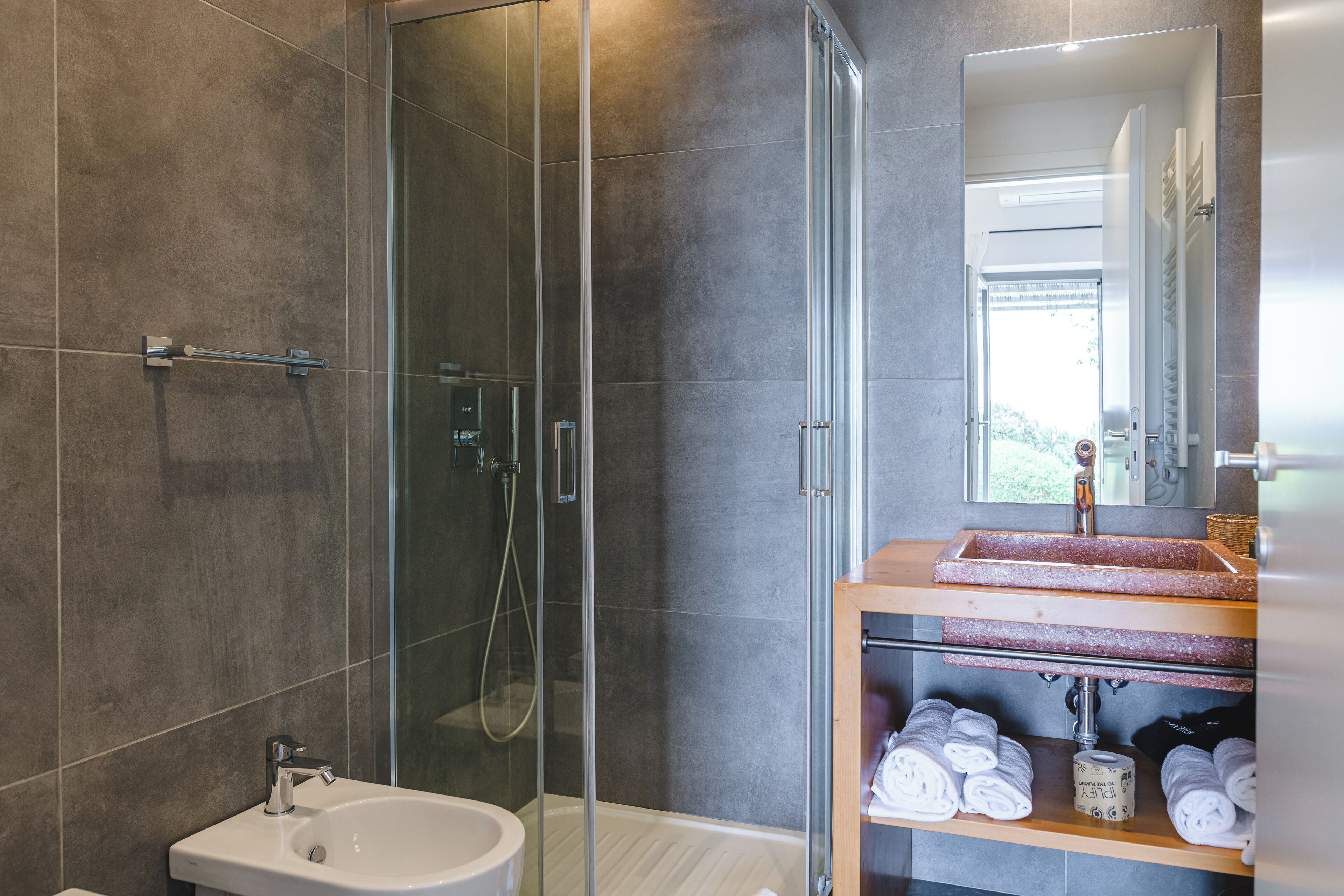 Une salle de bain moderne avec une douche à parois de verre, un lavabo blanc et un meuble-lavabo en bois agrémenté de serviettes.