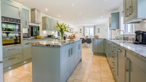 A modern kitchen with grey cabinets, a central island, and a dining area with chairs. - 5 Bed in Bradworthy (oc-d31987) (Bradworthy)