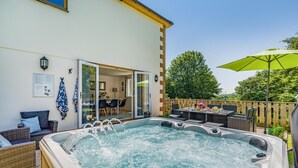 A hot tub in a backyard with a dining area and a covered patio. - 5 Bed in Bradworthy (oc-d31987) (Bradworthy)