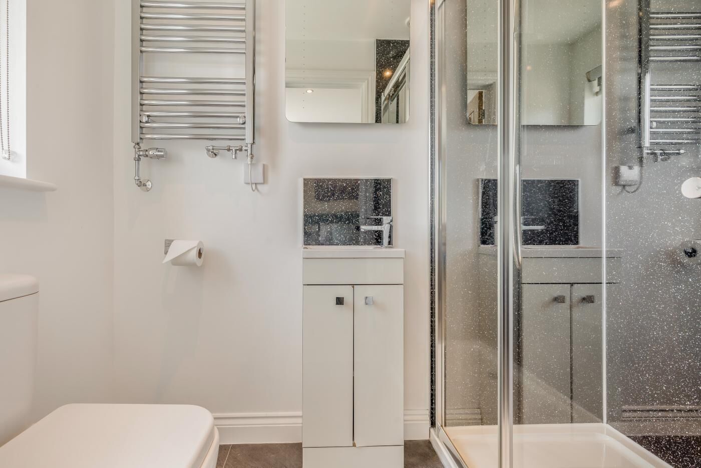 Un bany modern amb plat de dutxa de vidre, un lavabo blanc i un vàter.