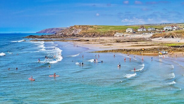 A coastal beach scene with waves, people, and buildings in the background. - 5 Bed in Bradworthy (oc-d31987) (Bradworthy)