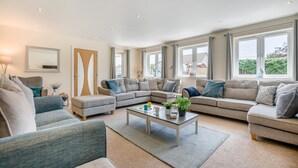 A spacious living room with a sectional sofa, a coffee table, and large windows providing natural light. - 5 Bed in Bradworthy (oc-d31987) (Bradworthy)