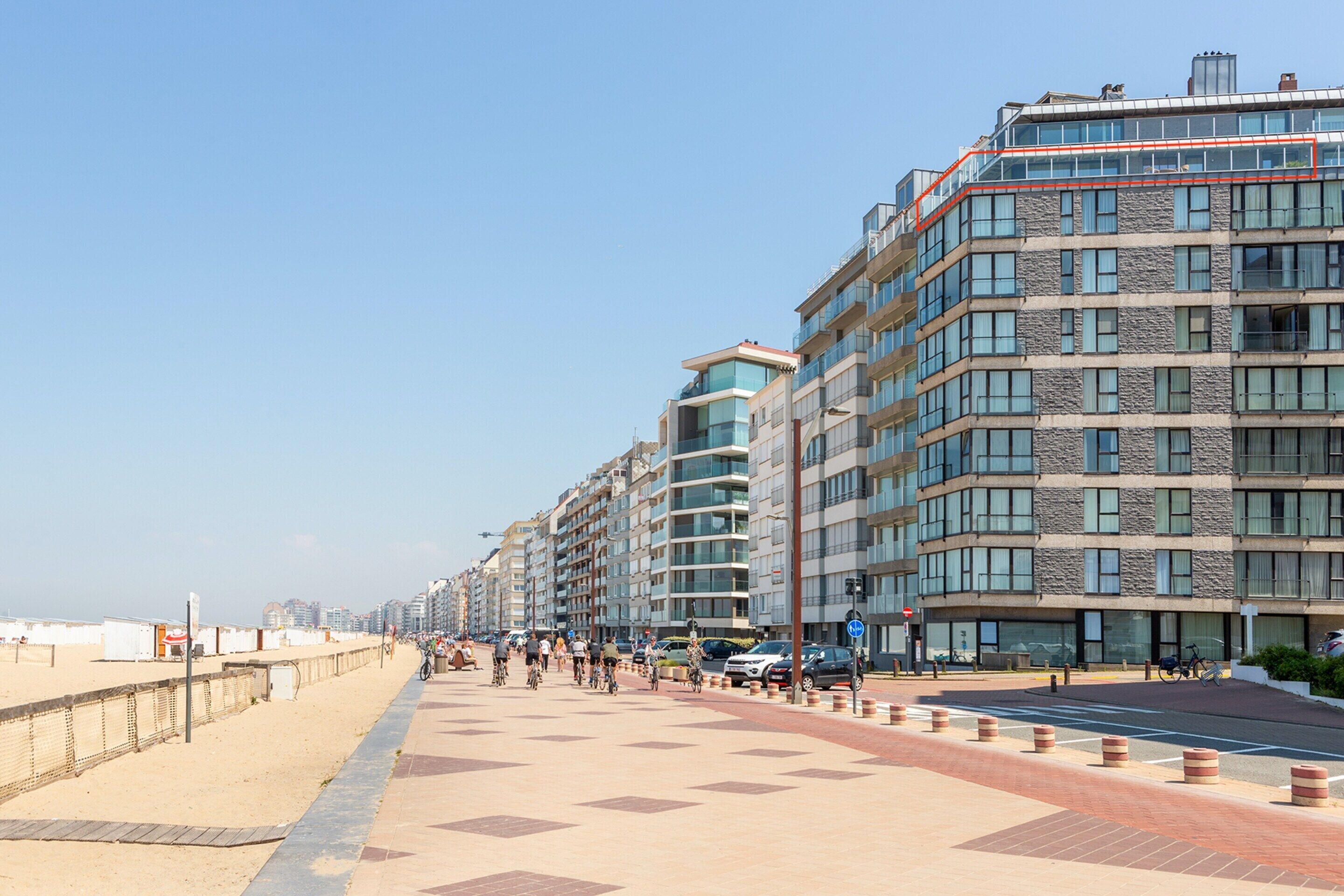 Un paseo marítimo con edificios modernos, una playa de arena y cielo despejado.