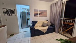 A living room with a sofa, a dining table, and a view through a sliding door. - APARTMENT SEA BRISE ARAÇAGY (Araçagi São José de Ribamar)
