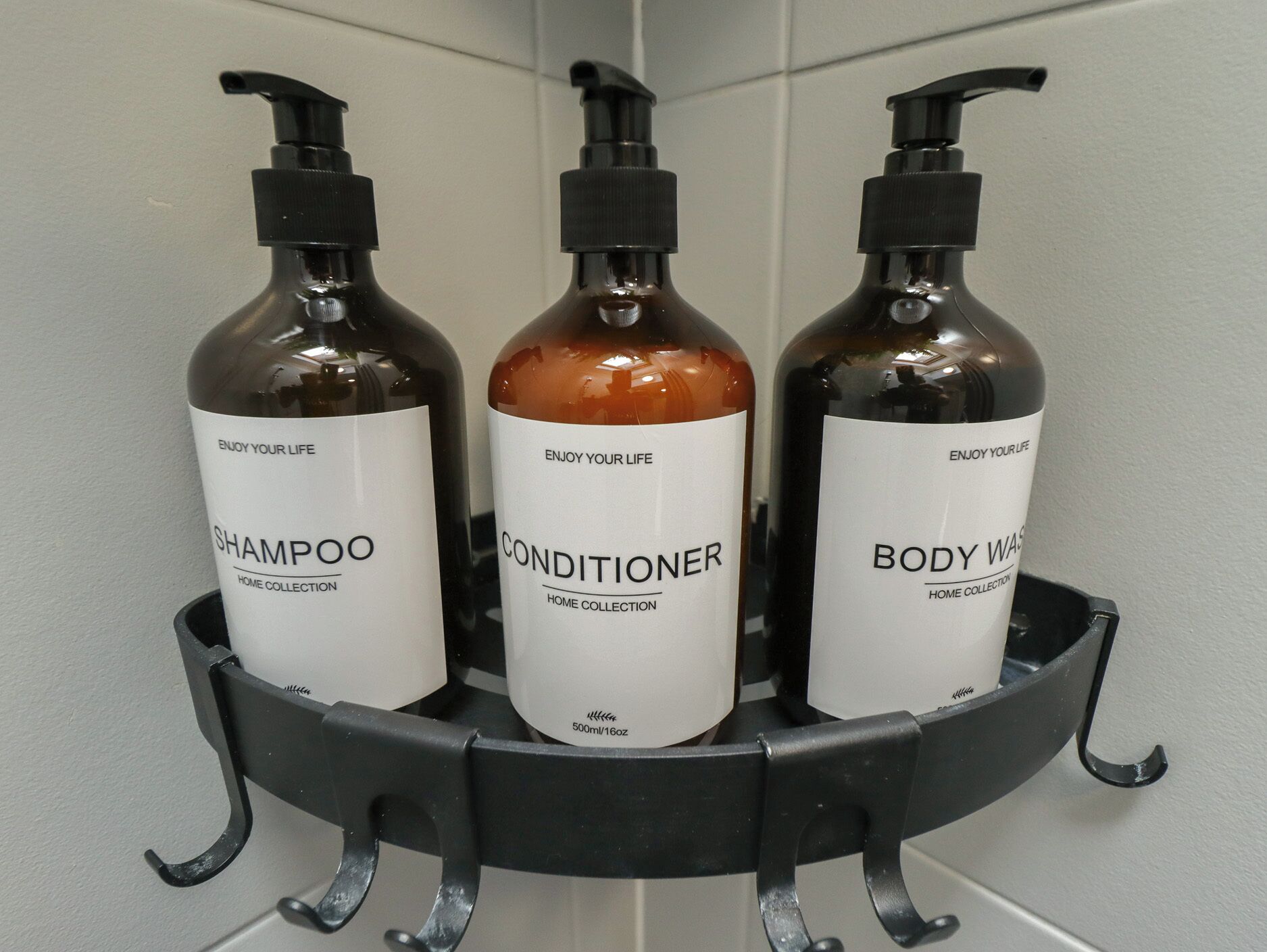Three bottles of shampoo, conditioner, and body wash on a black shelf.