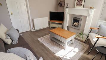 A living room with a sofa, a coffee table, a TV, a fireplace, and a bookshelf.