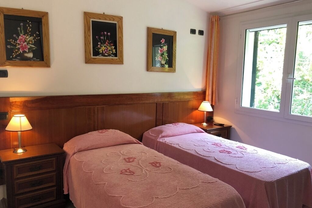 Quarto de hotel com duas camas, cabeceira de madeira, abajures e uma pintura floral emoldurada na parede.