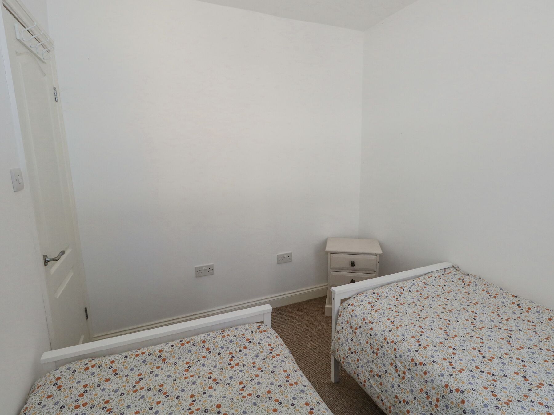 A small, sparsely furnished room with two single beds, a nightstand, and a door.