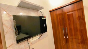 A flat-screen TV mounted on a marble wall, a wooden wardrobe with two doors, and a power outlet below the TV. - Shree Hari Niwas Paying Guest House (Varanasi)