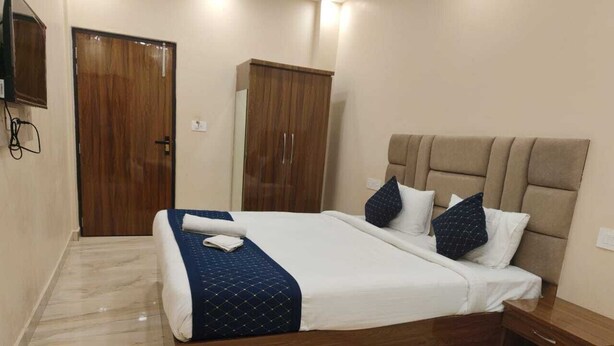 A bedroom with a bed, a wooden wardrobe, a bedside table, and a TV mounted on the wall. - Shree Hari Niwas Paying Guest House (Varanasi)