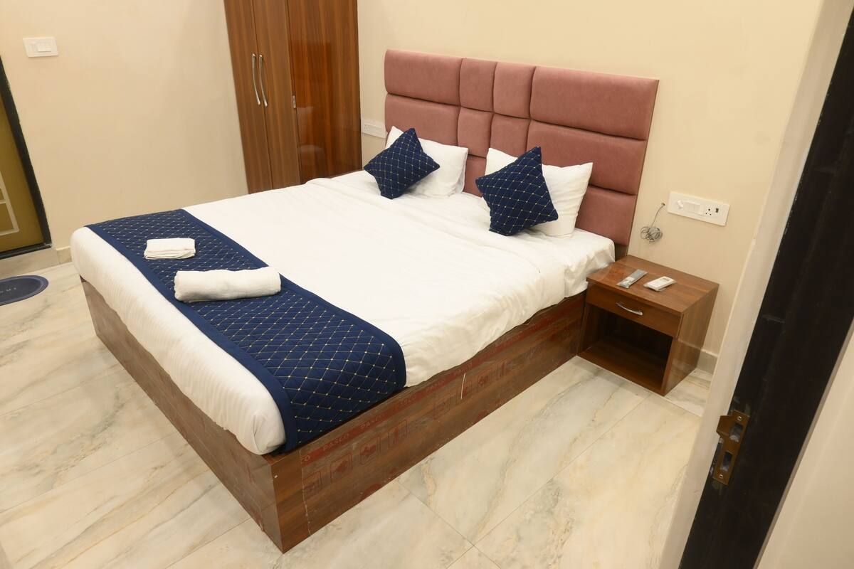 Una cama bien hecha con colcha azul, dos almohadas y una toalla doblada sobre un marco de madera.