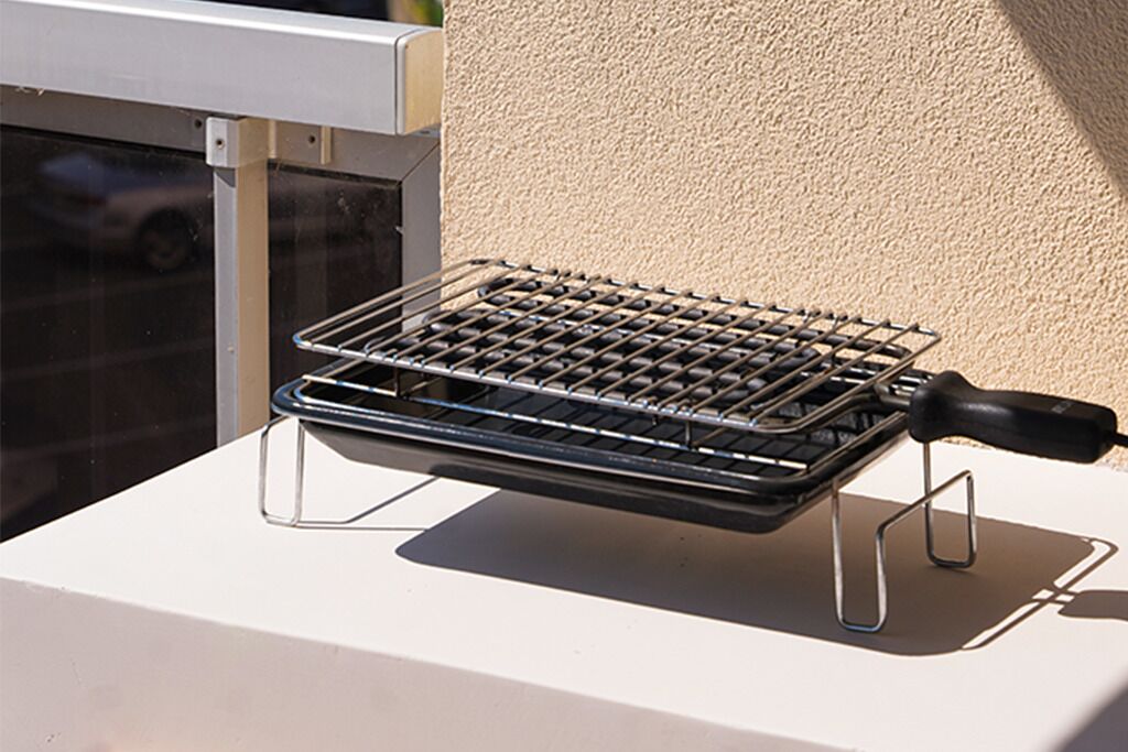 Ein tragbarer Grill auf einer weißen Oberfläche, im Hintergrund eine strukturierte Wand.