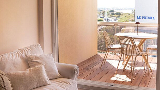 A balcony with a wooden floor, a beige sofa with cushions, and a table with chairs. - Le Calypso - Magnificent sea-view terrace - 100m from Le Boucanet beach (Le Grau-du-Roi)