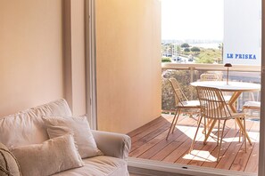 Un balcón con piso de madera, un sofá color beige con cojines y una mesa con sillas.