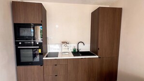 A compact kitchen with built-in appliances, a sink, and wooden cabinetry. - Le Calypso - Magnificent sea-view terrace - 100m from Le Boucanet beach (Le Grau-du-Roi)