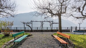 A park with benches, a gravel path, and a view of a lake and mountains. - Little Paradise - Lake Lugano View (San Mamete)