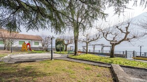 A park with a playground, benches, and a view of a body of water. - Little Paradise - Lake Lugano View (San Mamete)
