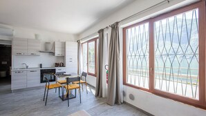 A modern kitchen with a dining area, large windows with a view of the sea, and a balcony with a metal railing. - Little Paradise - Lake Lugano View (San Mamete)