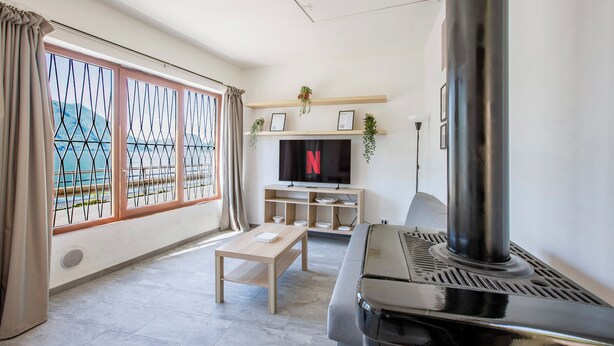 A living room with a TV, a fireplace, and a large window with curtains. - Little Paradise - Lake Lugano View (San Mamete)