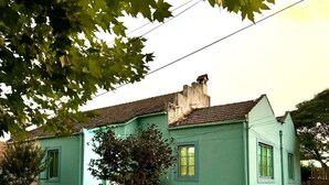 Een gelijkvloers huis met een lichtblauwe gevel, een zichtbare schoorsteen en een kleine voortuin met een houten hek.