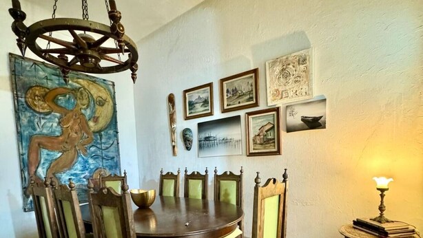 Een eetkamer met een houten tafel en stoelen, een kroonluchter en kunstwerken aan de muren.